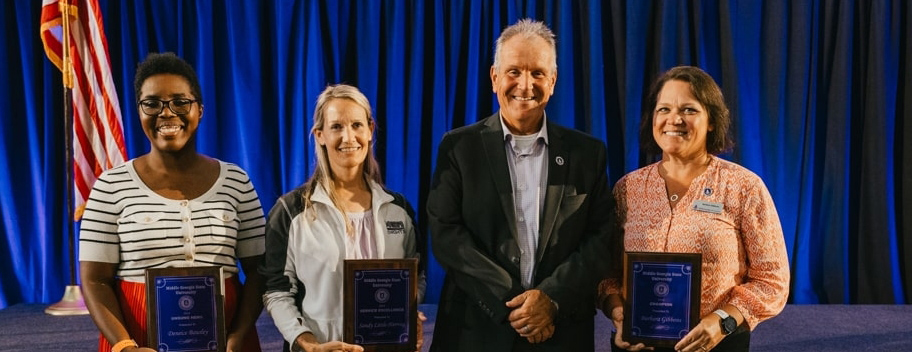 Staff Award winners Deneice Bausley, Sandy Little-Herring, and Barbara Gibbons smiling with President Blake